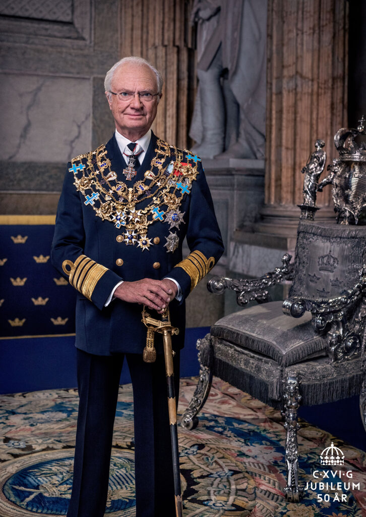 Kung Carl XVI Gustaf står framför en elegant stol. Han tittar rakt in i kameran och håller i ett svärd framför sig. Han har en mörkblå kostym och bär Serafimerordens, Svärdsordens, Nordstjärneorden och Vasaordens kedjor runt halsen. På bröstet, under kedjorna, bärs också de fyra kungliga minnestecken Kungen brukar bära: GV:sJmtII och GVIA:sMM i serafimerblått band samt norska HVII:sMM och OV:sMM i rött band. 