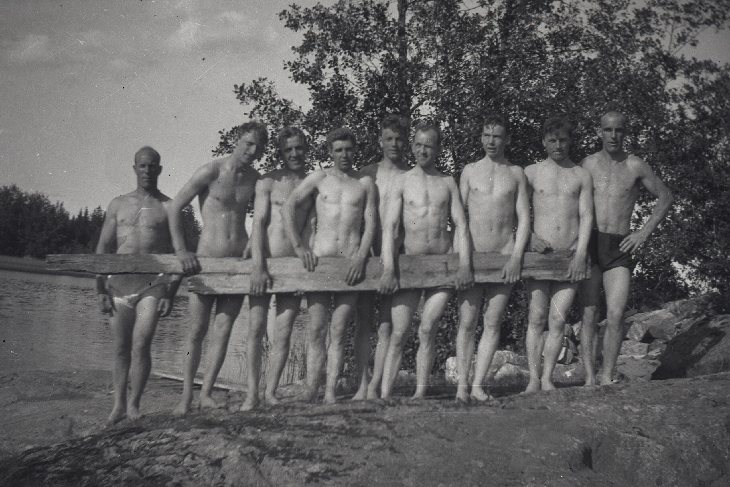 En grupp män med planka framför sig, vid sjö.