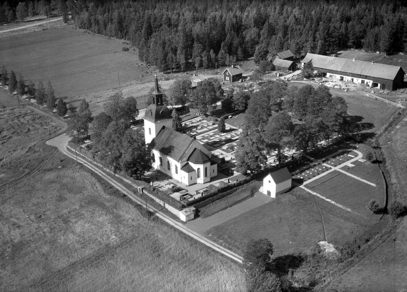 En svartvit flygbild över en kykra och dess kyrkogård.
