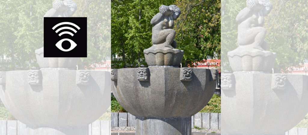 En stenstaty i en fontän föreställer en figur som sitter på huk och håller en snäcka mot örat. Bakom syns gröna träd. I bildens vänstra hörn finns en svart symbol med ett öga och radiovågor ovanför.