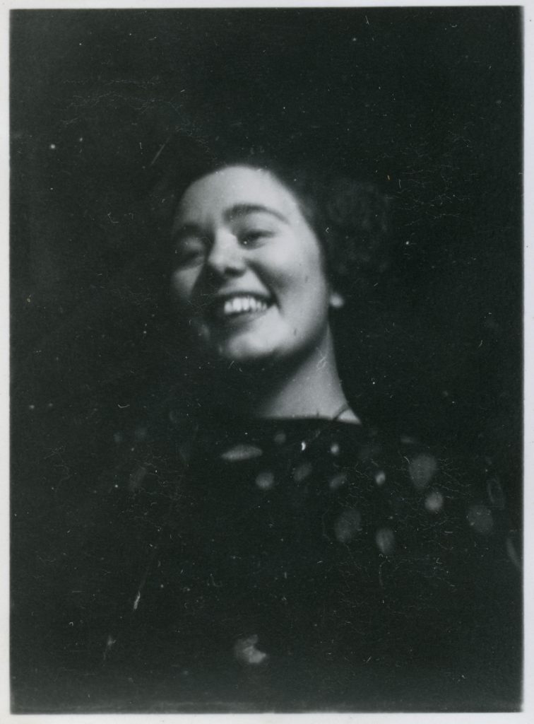 Svartvitt fotografi av en ung kvinna som ler brett mot kameran. Bilden är något oskarp och tagen i närbild.